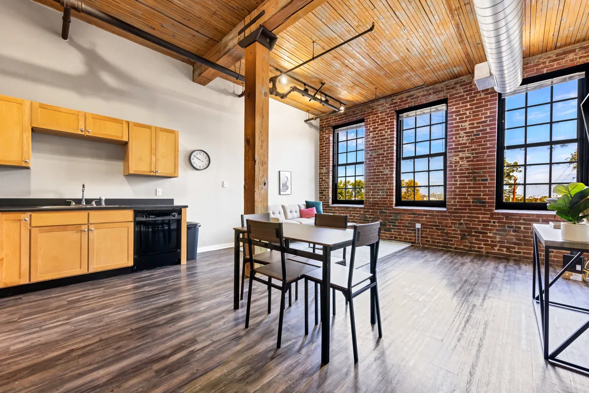 This image features a chef-inspired kitchen area seamlessly connected to a dining table set beside large windows and an exposed brick wall. The kitchen is equipped with modern appliances, and the inviting dining nook is illuminated by statement lighting. Visible activities include dining, social gatherings, cooking, and relaxing. The mood is welcoming and cozy, and the space captures morning coffee rituals as well as dinner parties with friends.