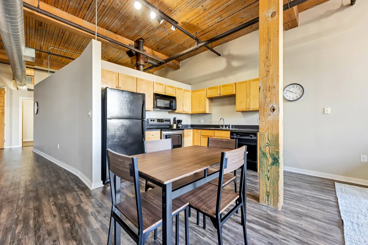 A cozy kitchen and dining space highlighting modern appliances and a welcoming table set beneath warm lighting. Wooden beams accentuate the historic charm, while the area is arranged for activities such as cooking, dining, and entertaining. The scene conveys sharing meals and celebrating special occasions in a comfortable setting.