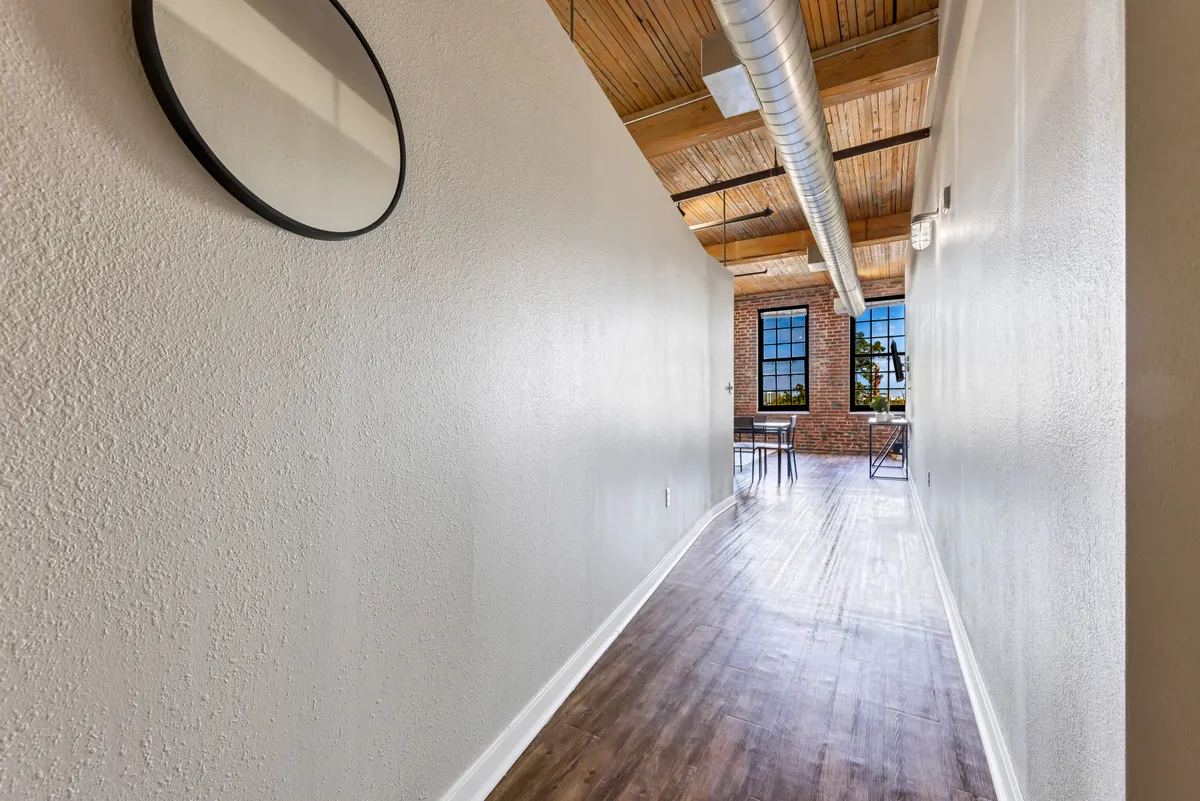 A well-lit interior scene with exposed beams, a brick wall, and a large window, including a mirror and subtle storage elements. The inviting atmosphere suggests a home designed for both comfort and organization, with areas that could easily integrate versatile storage solutions.
